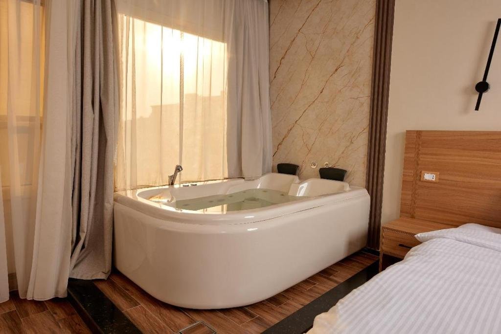 White Jacuzzi bathtub next to a large window with sheer curtains in a hotel room